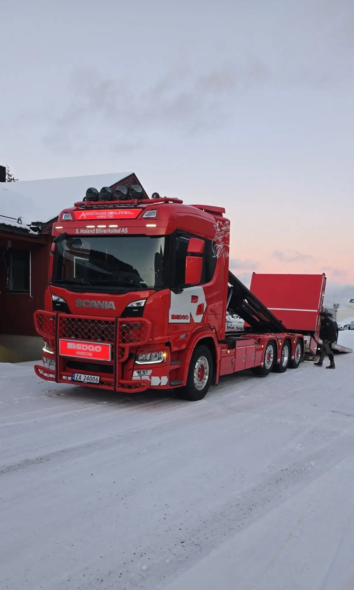 Rød Scania kranbil i vinterlys utenfor verkstedet ved skumring