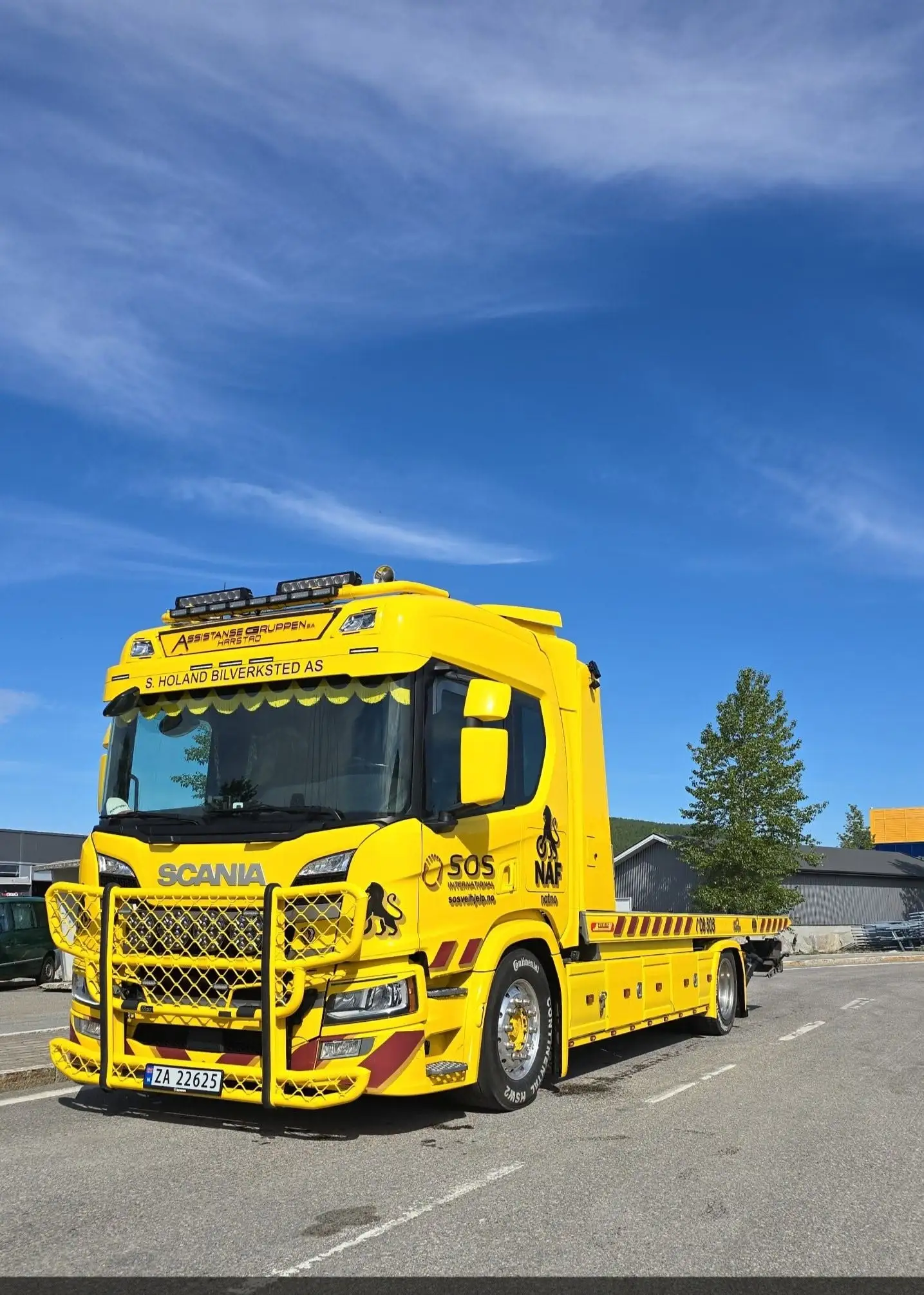 Gul Scania bergingsbil med tomt lasteplan i strålende solskinn